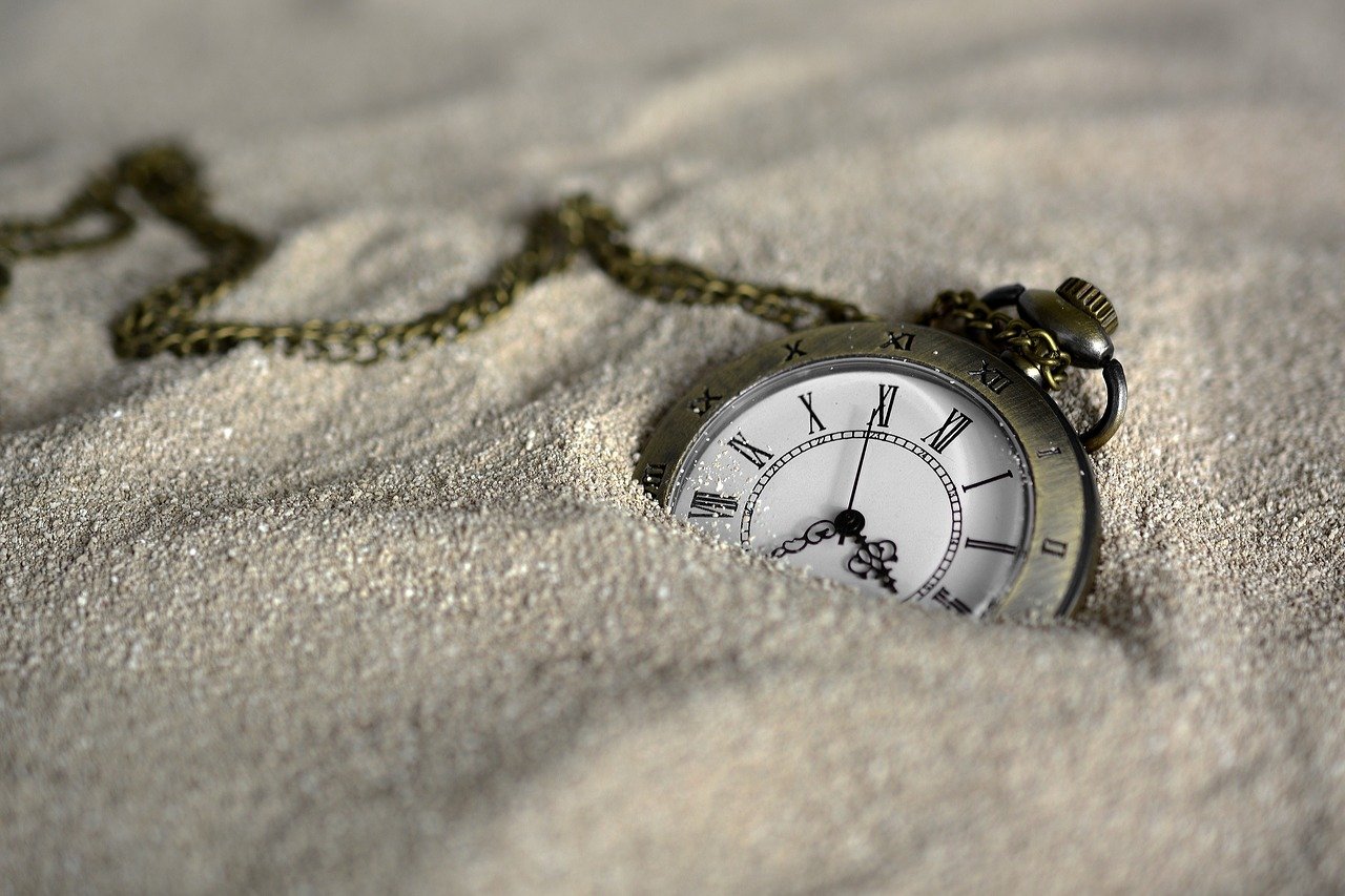 An image of a pocket watch laying in sand.